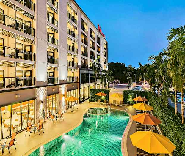 Bygning med flere etager, grøn pool og parasoller ved siden af. (AI-genereret tekst)