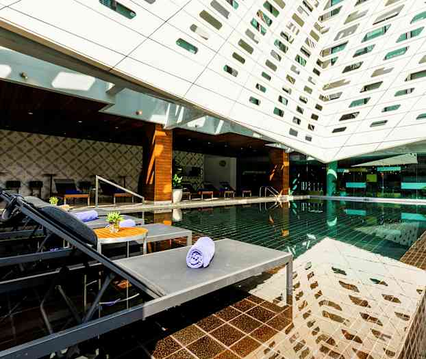 Et moderne udendørsområde med en pool, liggestole og et tag dækket af geometriske åbninger. (AI-genereret tekst)