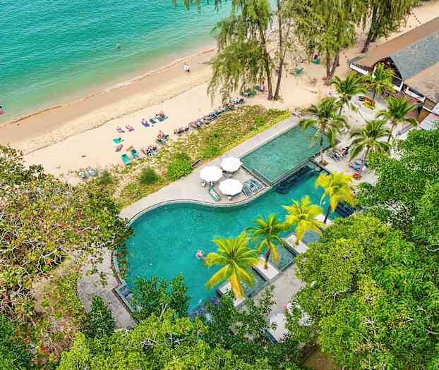 Luftfoto af en strand med liggestole og et poolområde omgivet af grønt. (AI-genereret tekst)