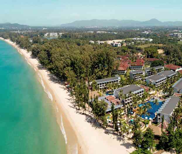 Luftfoto af en ferieby ved en strand med omkringliggende træer og bygninger. (AI-genereret tekst)