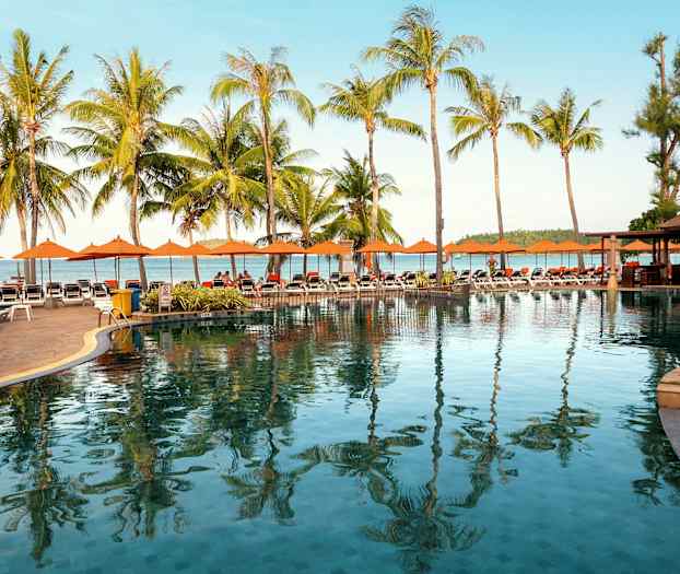 Poolområde med liggestole, palmer og hav i baggrunden. (AI-genereret tekst)