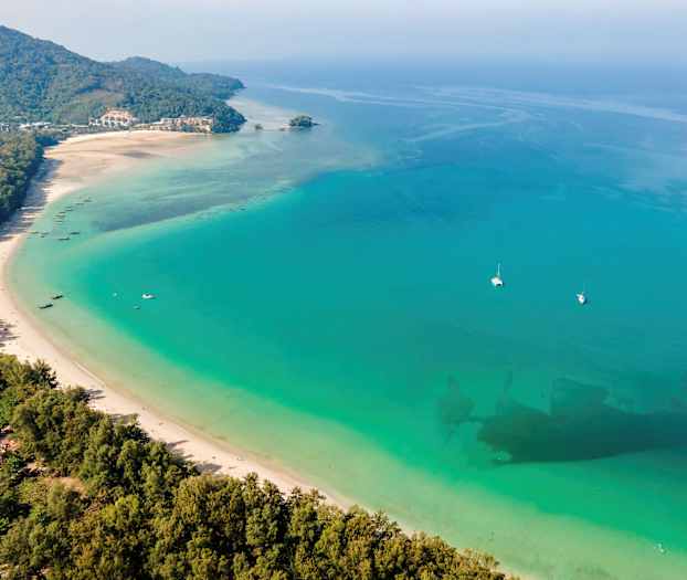 Lang hvid sandstrand mod turkisblåt hav med både og frodige omgivelser. (AI-genereret tekst)