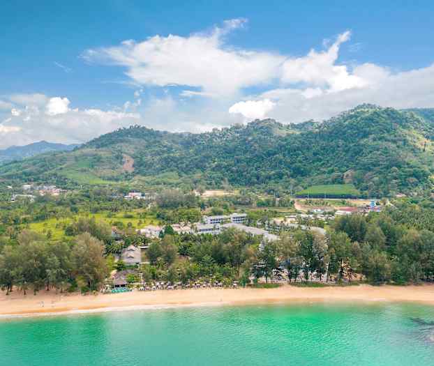 Landskab med en strand, frodige bakker og bygninger ved vandet. (AI-genereret tekst)