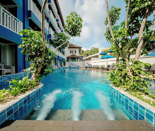 En pool med frodige planter omgivet af bygning og liggestole. (AI-genereret tekst)