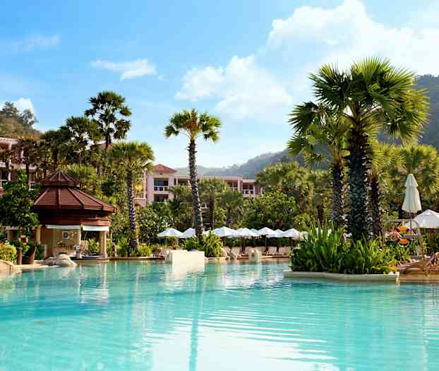 En pool omgivet af høje palmer, liggestole med parasoller og bygninger omkranset af beplantning. (AI-genereret tekst)