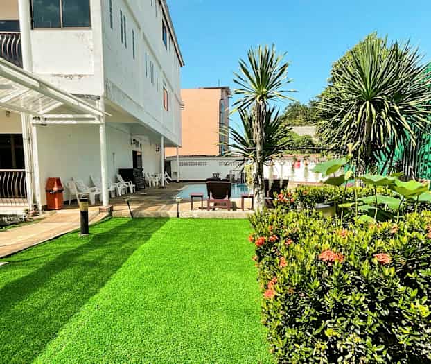 Et udendørs billede af en bygning med en grøn plæne og omkringliggende planter. (AI-genereret tekst)