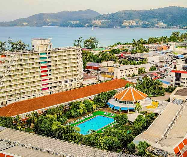 Udsigt over et hotelområde med en hvid bygning i flere etager, en swimmingpool og udsigt mod havet. (AI-genereret tekst)