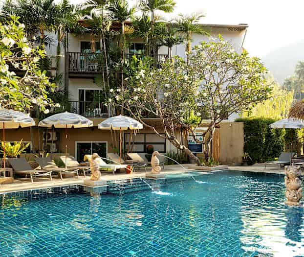 Poolområde med parasoller og liggestole foran et hotel. (AI-genereret tekst)