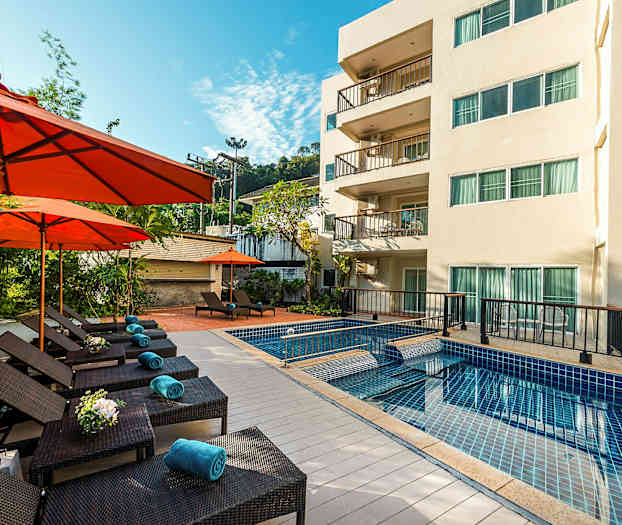 Udendørs swimmingpool med liggestole og orange parasoller ved siden af en treetagers bygning. (AI-genereret tekst)