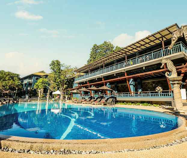 Udendørs pool ved et hotel med liggestole og omkringliggende træer. (AI-genereret tekst)