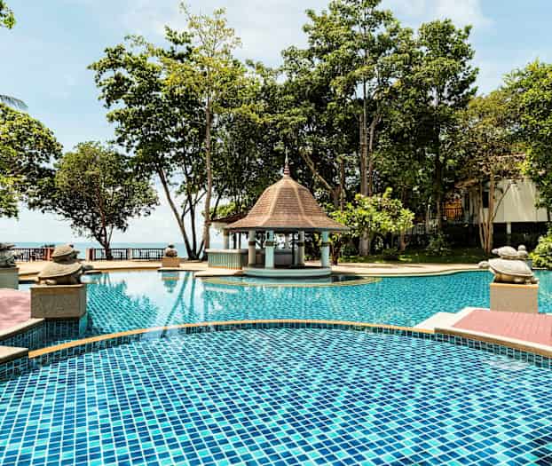 En pool ved et hotelområde omgivet af træer, med et lille pavillonlignende tag og dekorationer i form af skildpadder ved kanten. (AI-genereret tekst)