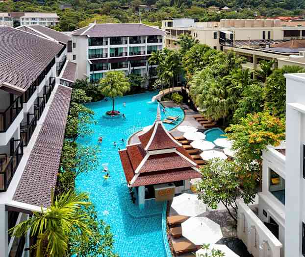 Lyst billede af et hotelområde med en stor pool omgivet af grønne træer og bygninger med brune tage. (AI-genereret tekst)