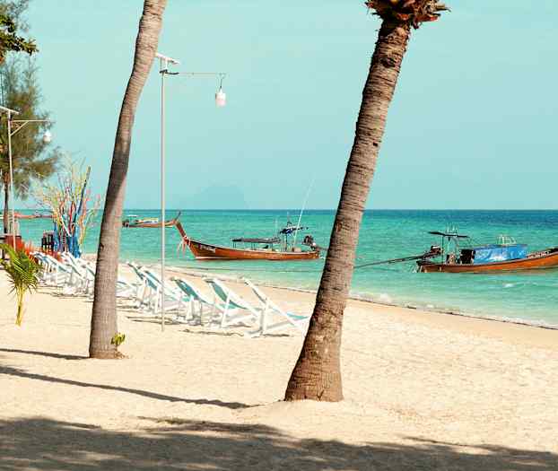 Strand med palmer, liggestole og traditionelle træbåde i havet. (AI-genereret tekst)