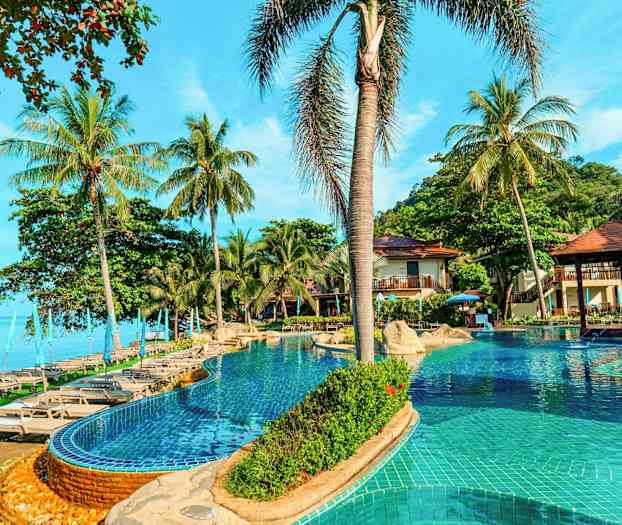 En pool med liggestole og parasoller omgivet af palmer ved siden af havet. (AI-genereret tekst)