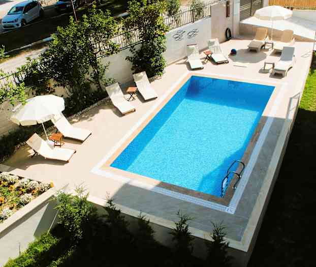 En rektangulær pool med liggestole og parasoller ved siden af. (AI-genereret tekst)