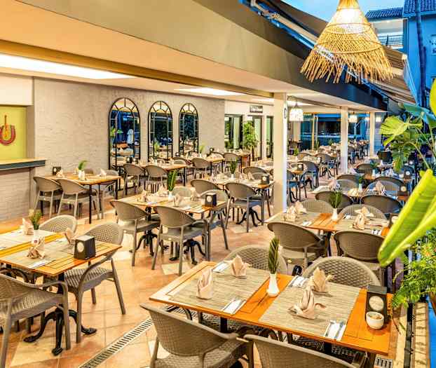 En restaurantmiljø med oprettede borde og stole, dekoreret med planter og velplacerede servietter. (AI-genereret tekst)