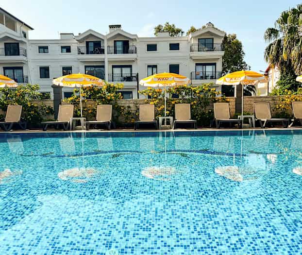 En pool med liggestole og gule parasoller foran en lejlighedsbygning. (AI-genereret tekst)