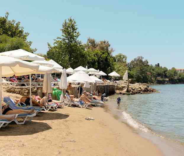 Badestrand med liggestole og parasoller ved kanten af klart vand. (AI-genereret tekst)