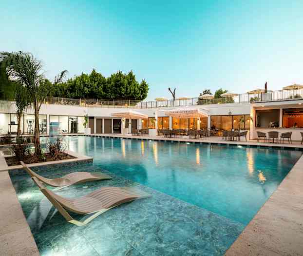 Udendørs pool med liggestole og restaurant i baggrunden. (AI-genereret tekst)