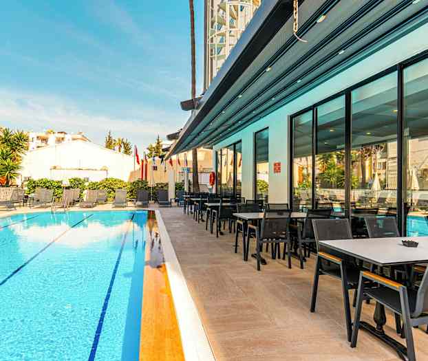En hotelpool med liggestole og et tilstødende spiseområde. (AI-genereret tekst)