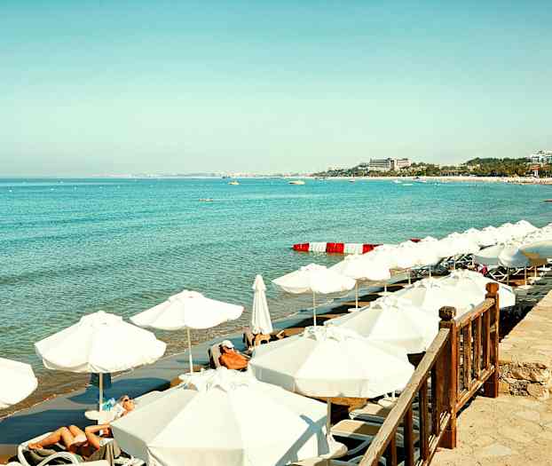 Hvid sandstrand med liggestole og parasoller ved klart blåt hav. (AI-genereret tekst)