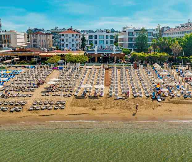 Strand med liggestole og parasoller, omgivet af hoteller og bygninger. (AI-genereret tekst)