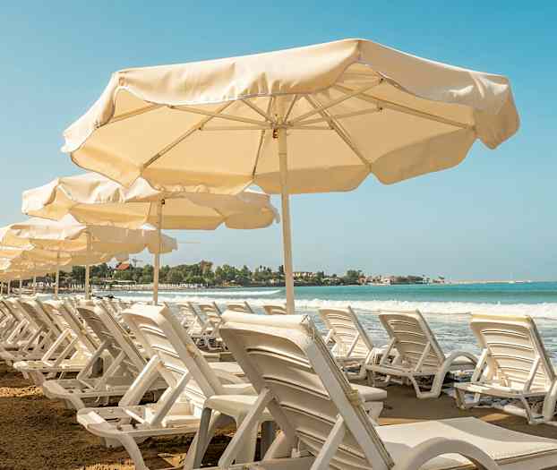 Række af liggestole og parasoller ved en sandstrand med havudsigt. (AI-genereret tekst)