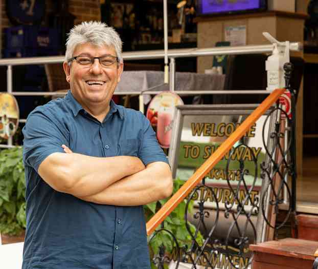 En person står med armene krydset foran en restaurantindgang med et velkomstskilt. (AI-genereret tekst)