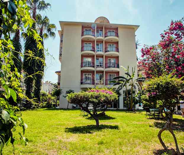 En lejlighedsbygning med altaner omgivet af grønt og blomstrende træer i forgrunden. (AI-genereret tekst)