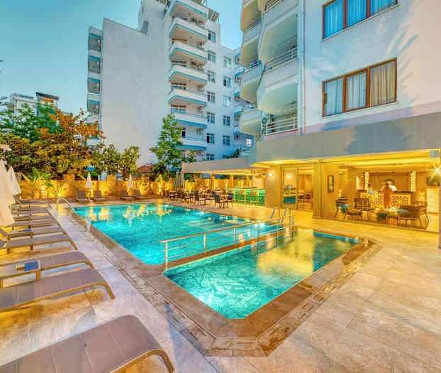 Udendørs pool med liggestole og parasoller, omgivet af bygninger. (AI-genereret tekst)