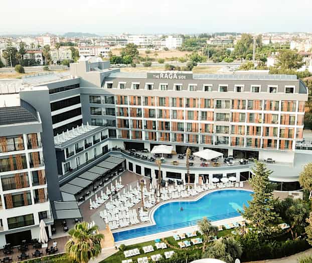 Luftfoto af hotelbygning med poolområde og liggestole foran. (AI-genereret tekst)