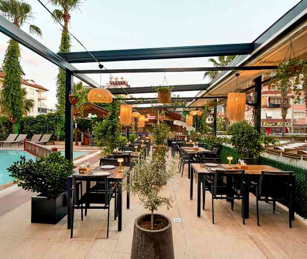 Udendørsrestaurant ved en pool med borde og stole samt planter og belysning. (AI-genereret tekst)