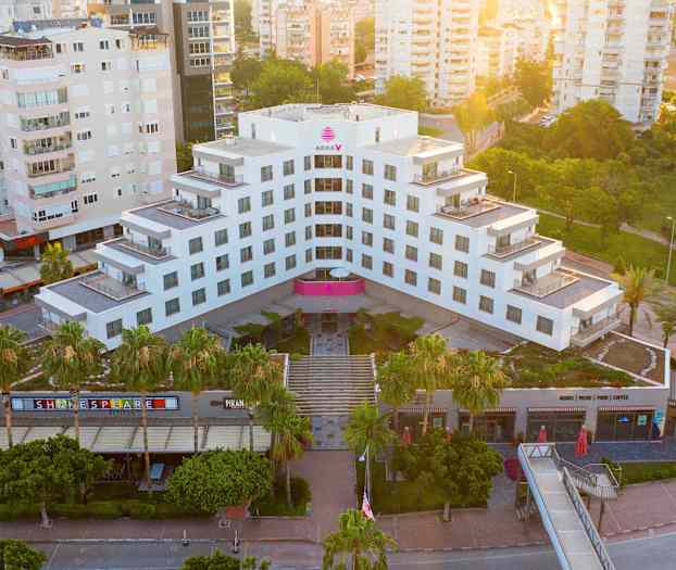 Et moderne hotel omgivet af grønt og andre bygninger, set ovenfra. (AI-genereret tekst)
