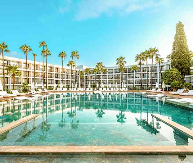 Hotelpool med liggestole og parasoller omgivet af palmer og moderne bygninger. (AI-genereret tekst)