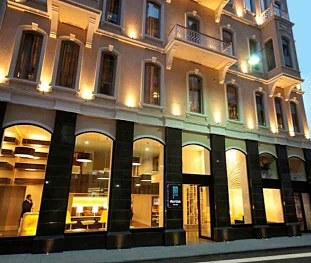 Udvendigt af et oplyst hotel med store vinduer. (AI-genereret tekst)