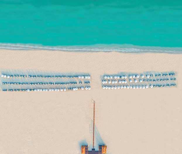 Luftfoto af en strand med liggestole og parasoller ved havet. (AI-genereret tekst)