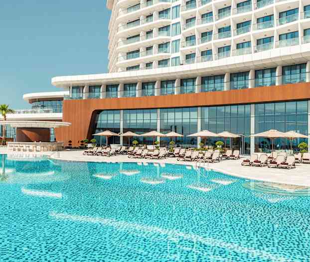 Et hotelkompleks med en stor pool foran, omgivet af liggestole og parasoller. (AI-genereret tekst)