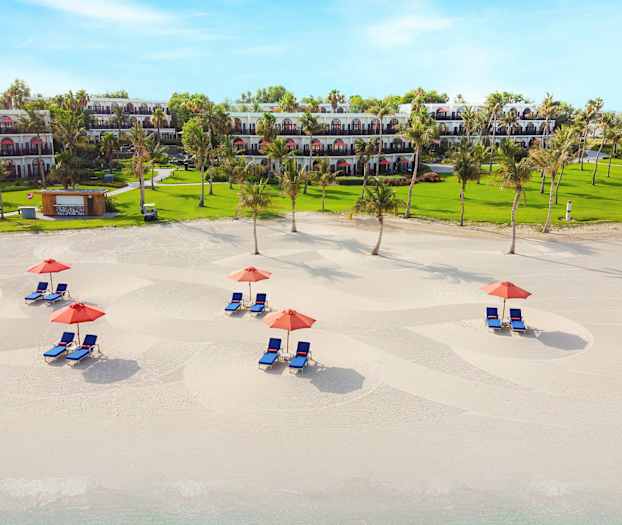 En sandstrand med liggestole og parasoller, grønne områder og bygninger i baggrunden. (AI-genereret tekst)