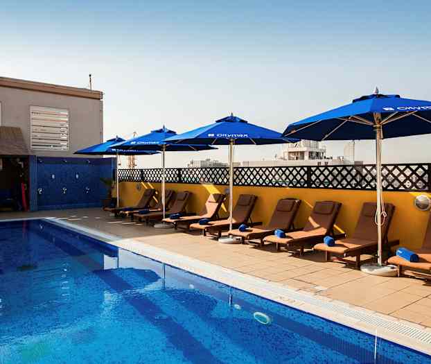 En pool med liggestole og parasoller ved siden under en klar himmel. (AI-genereret tekst)