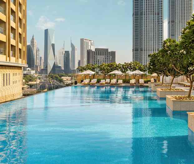 En infinitypool omgivet af liggestole og parasoller, med høje bygninger i baggrunden. (AI-genereret tekst)