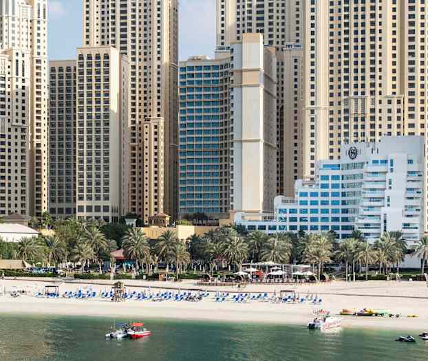 Høje bygninger i baggrunden med en strand foran samt palmer. (AI-genereret tekst)