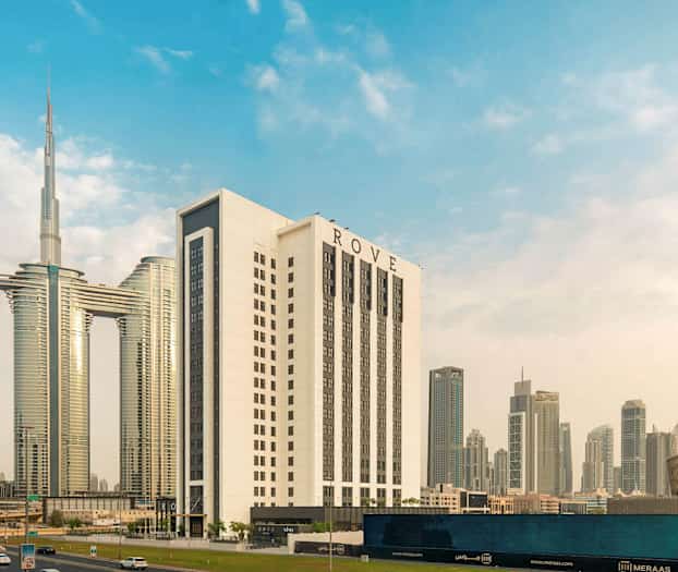 Et moderne bybillede med flere høje bygninger, herunder et større hvidt hotel med navnet ROVE, omgivet af andre skyskrabere og arkitektoniske strukturer. (AI-genereret tekst)