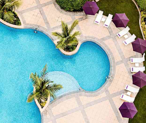 En udendørs swimmingpool med stole og lilla parasoller omkring. (AI-genereret tekst)