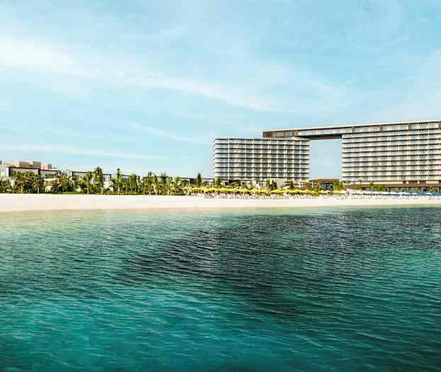 Udsigt over et hotel nær en sandstrand med klart vand. (AI-genereret tekst)