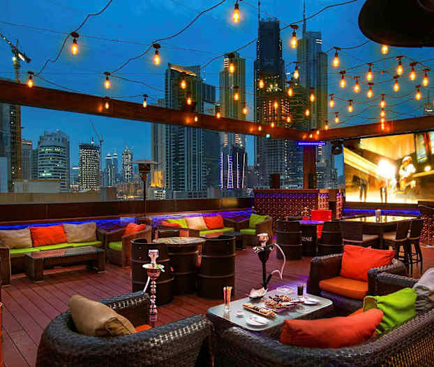 En tagterrasse med siddeområder, dekorative lamper og udsigt over en bysilhuet om aftenen. (AI-genereret tekst)