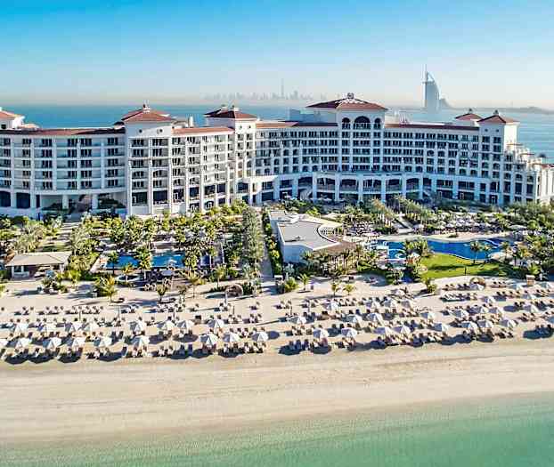 Et stort feriested med pools, liggestole og en hvid sandstrand ved havet. (AI-genereret tekst)