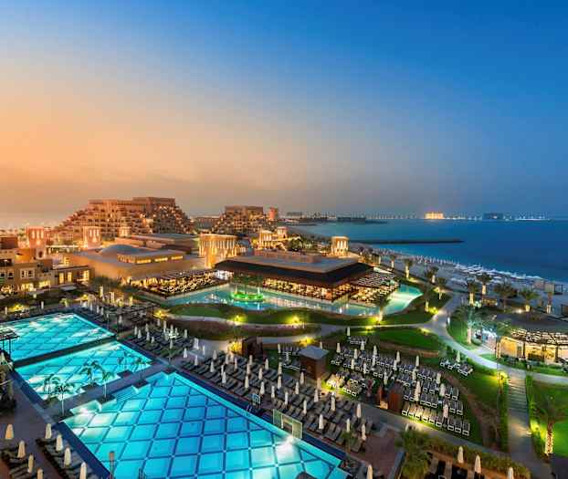 Udsigt over et hotelområde med bygninger, swimmingpools og strand ved havet. (AI-genereret tekst)