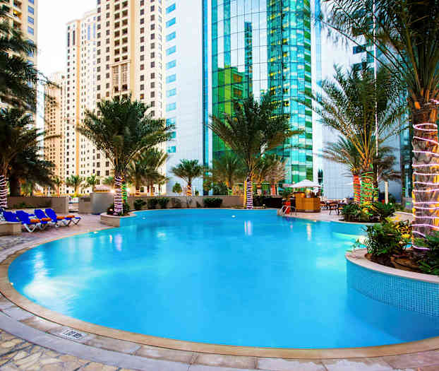 En udendørs pool omgivet af palmer med højhuse i baggrunden. (AI-genereret tekst)