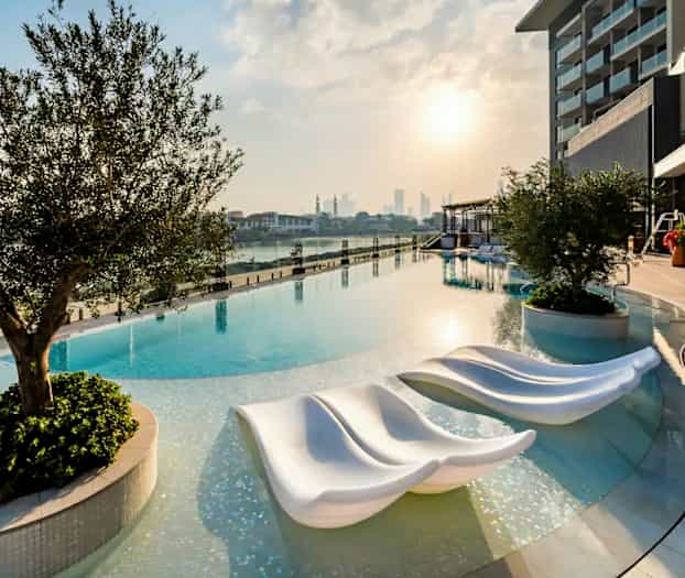 Billede af en infinitypool ved solnedgang med moderne solsenge og omgivelser med beplantning. (AI-genereret tekst)