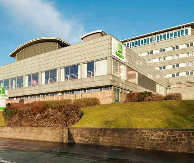 Holiday Inn-hotel i en moderne bygning omgivet af græsplæne og buske. (AI-genereret tekst)